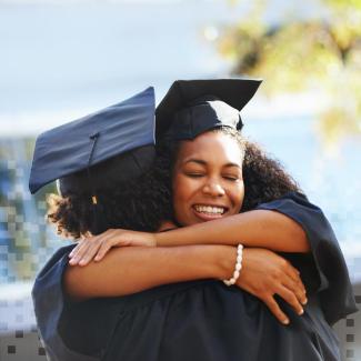 Two African American adults hug joyfully, wearing graduation caps and gowns 