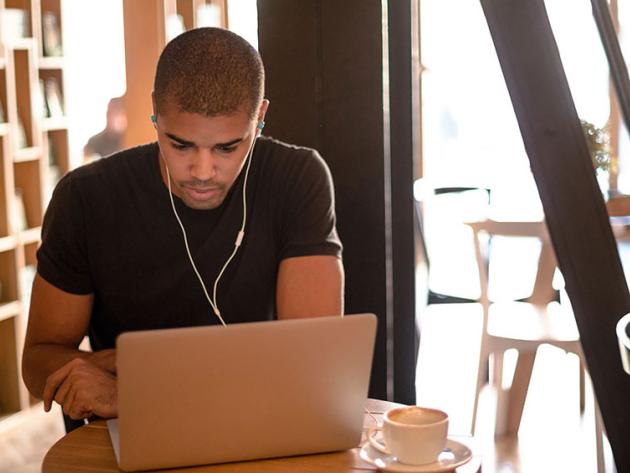 Man wearing earbuds and studying at laptop